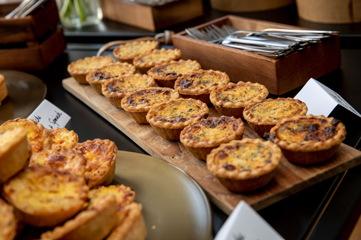 Mini quiches arranged on wooden tray with cutlery nearby