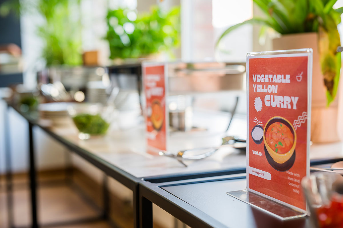 Buffet table with vegan curry sign and serving utensils