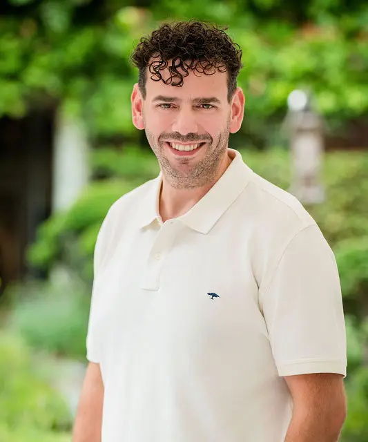 white man with dark hair smiling with white polo shirt