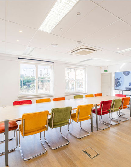 Room with long table, colorful chairs, screen
