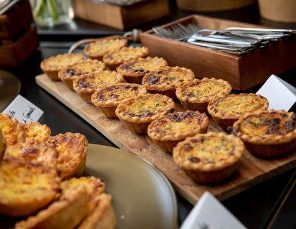 Mini quiches arranged on wooden tray with cutlery nearby